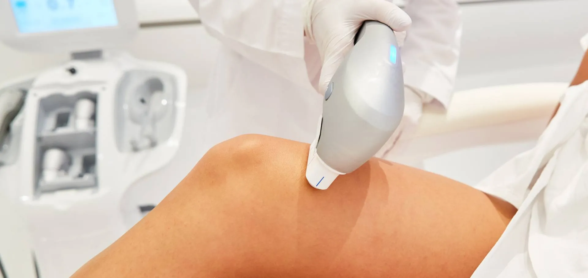 Aplicação de equipamento de estética corporal em paciente deitada, ambiente clínico moderno, tons neutros dessaturados, fotografia editorial